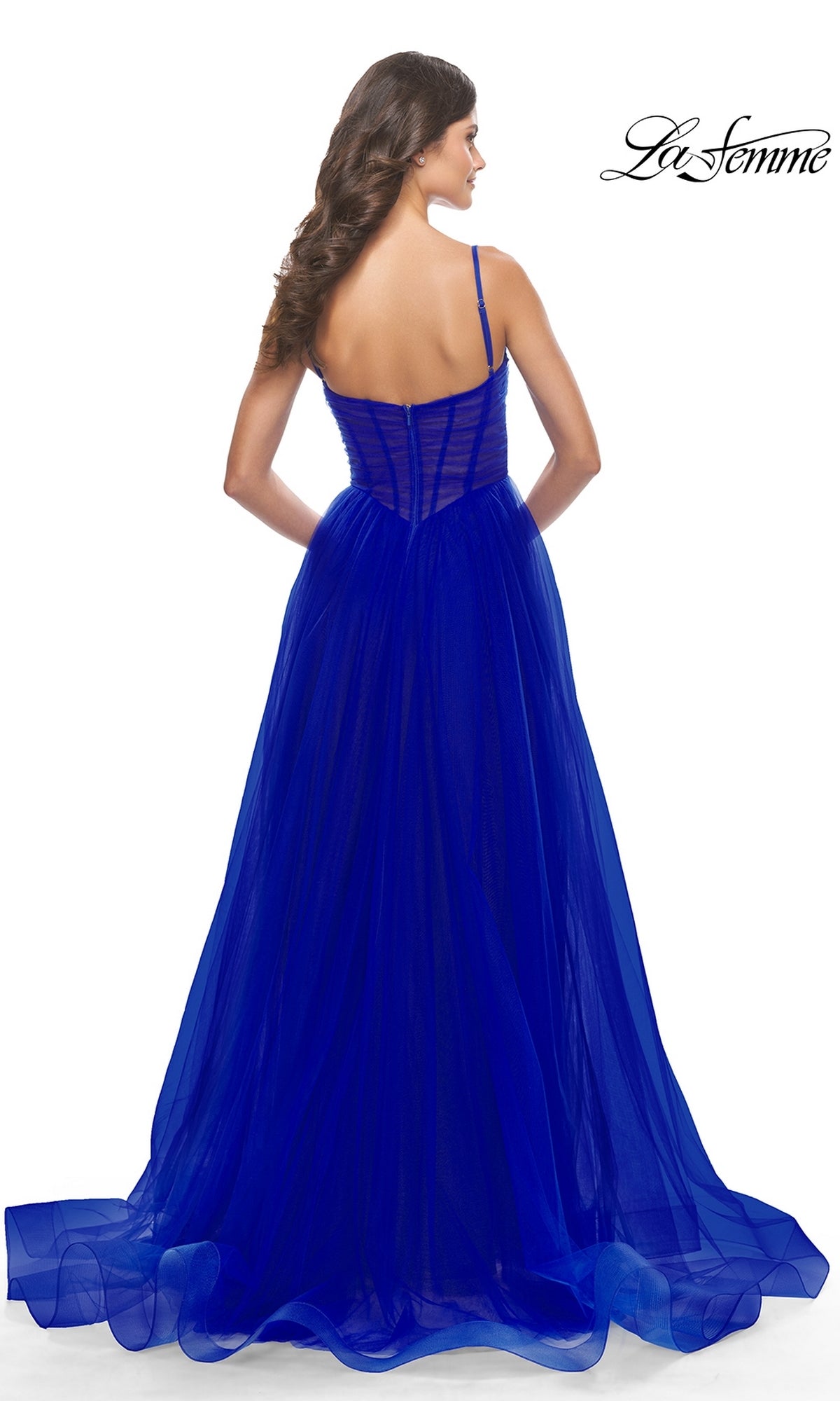 A woman models the Sheer-Waist La Femme Long Prom Ball Gown 31147 in royal blue, showing the elegant back details of the floor-length formal dress with spaghetti straps and a sheer overlay. The La Femme logo is visible in the corner.